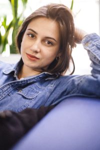 Woman Sitting On A Couch In A Denim Jacket Learning About Pregnancy Services